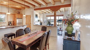 Una cocina amplia con vigas de madera, un comedor con mesa y sillas de madera, y vistas al exterior a través de amplios ventanales.