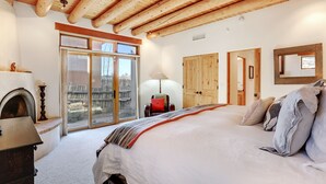 Un dormitorio con una cama grande, vigas de madera en el techo, una chimenea y una puerta corredera de vidrio al exterior.