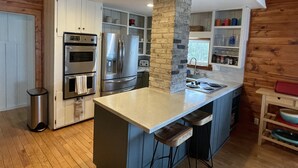A modern kitchen with stainless steel appliances, a central island, and wooden accents. - Lake Michigan Cottage w/ 265 ft of Private Beachfront! Perfect family getaway!  (Manistee)