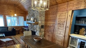 A wooden interior with a large dining table, benches, a stone fireplace, and a kitchen area. - Lake Michigan Cottage w/ 265 ft of Private Beachfront! Perfect family getaway!  (Manistee)