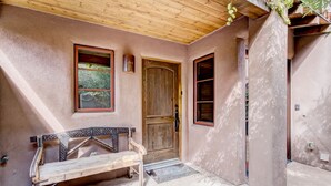 A rustic exterior with a wooden bench, a wooden door, and a window with a view of greenery. - El Corazon de Santa Fe | Patios, Private Balcony (Santa Fe)