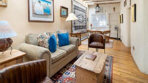 A cozy living room with a sofa, armchair, and coffee table. There is a dining area with a table and chairs, and a door leading to another room.