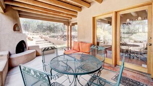 An outdoor patio with a round metal table and chairs, a stone fireplace, and a view of a landscaped garden. - Moonstar | Pet Friendly, Rooftop Deck, 360 Views! (Santa Fe)