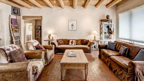 A cozy living room with wooden beams, leather sofas, a wooden coffee table, and a bookshelf with decorative items. - Moonstar | Pet Friendly, Rooftop Deck, 360 Views! (Santa Fe)