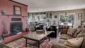 A living room with a fireplace, leather chairs, a sofa, and a kitchen in the background. - Sunset Haven | Mountain Views, Shuffleboard! (Santa Fe)