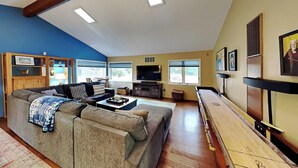 A living room with a sectional sofa, a flat-screen TV, a wooden coffee table, and a shuffleboard table. - Sunset Haven | Mountain Views, Shuffleboard! (Santa Fe)