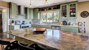 A modern kitchen with green cabinets, a large marble island, and pendant lighting. - Sunset Haven | Mountain Views, Shuffleboard! (Santa Fe)