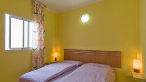Een hotelkamer met een bed, twee bedlampen, een raam met gordijn en een wandlamp.