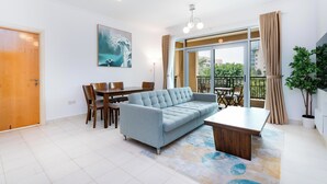 A modern living room with a sofa, dining table, chairs, and a large window with a view of the outdoors.