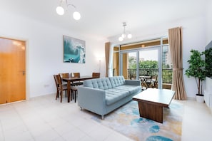 A modern living room with a sofa, dining table, chairs, and a large window with a view of the outdoors.