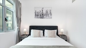 A neatly made bed with a grey blanket, two bedside lamps, and a wall-mounted picture of horses.