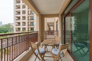 A balcony with a wooden table and chairs, a glass door, and a view of a high-rise building.