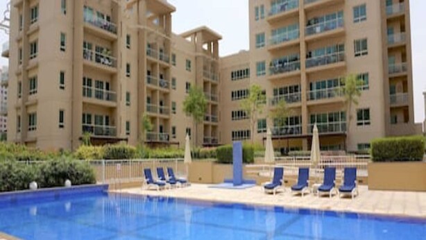 A swimming pool with lounge chairs and a building with multiple floors and balconies in the background.