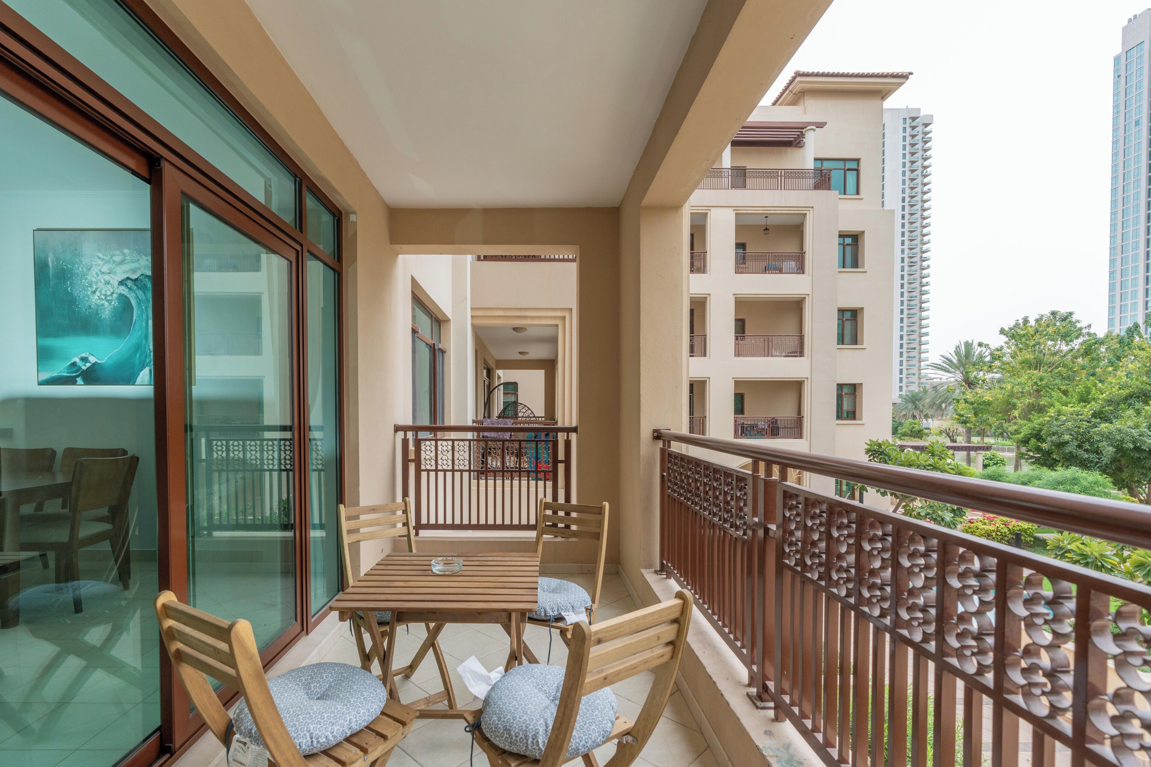 Un balcone con tavolo e sedie, vista sull'interno dell'edificio e scorcio del verde circostante.