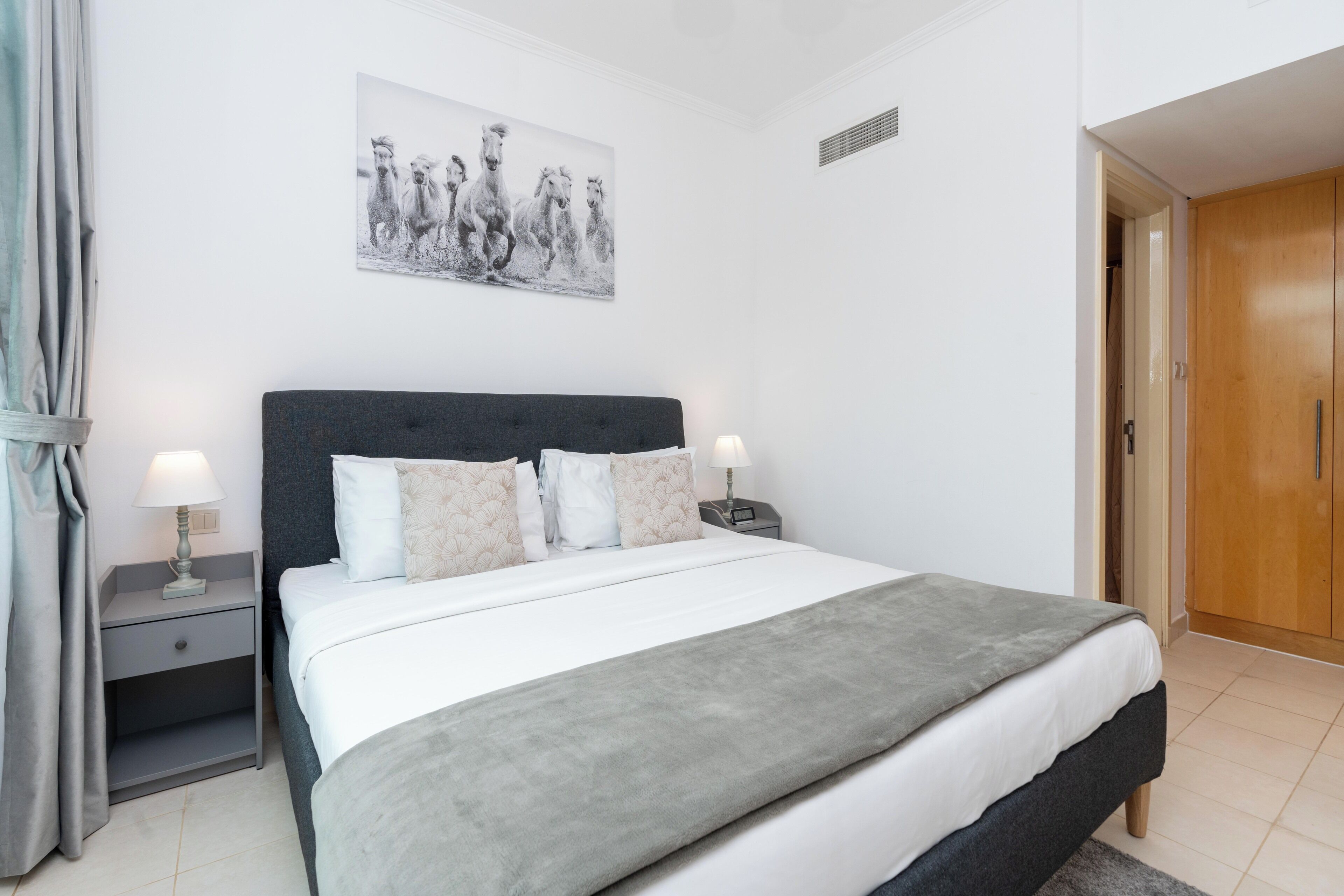 Quarto com cama, mesas de cabeceira, luminária, pintura e armário.