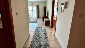A hallway with a patterned rug, a bench, a door, and a view to an outdoor area with a table and chairs.