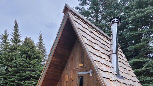 Una cabaña de madera con techo a dos aguas, una chimenea y un pequeño porche con escalones que conducen a la entrada.