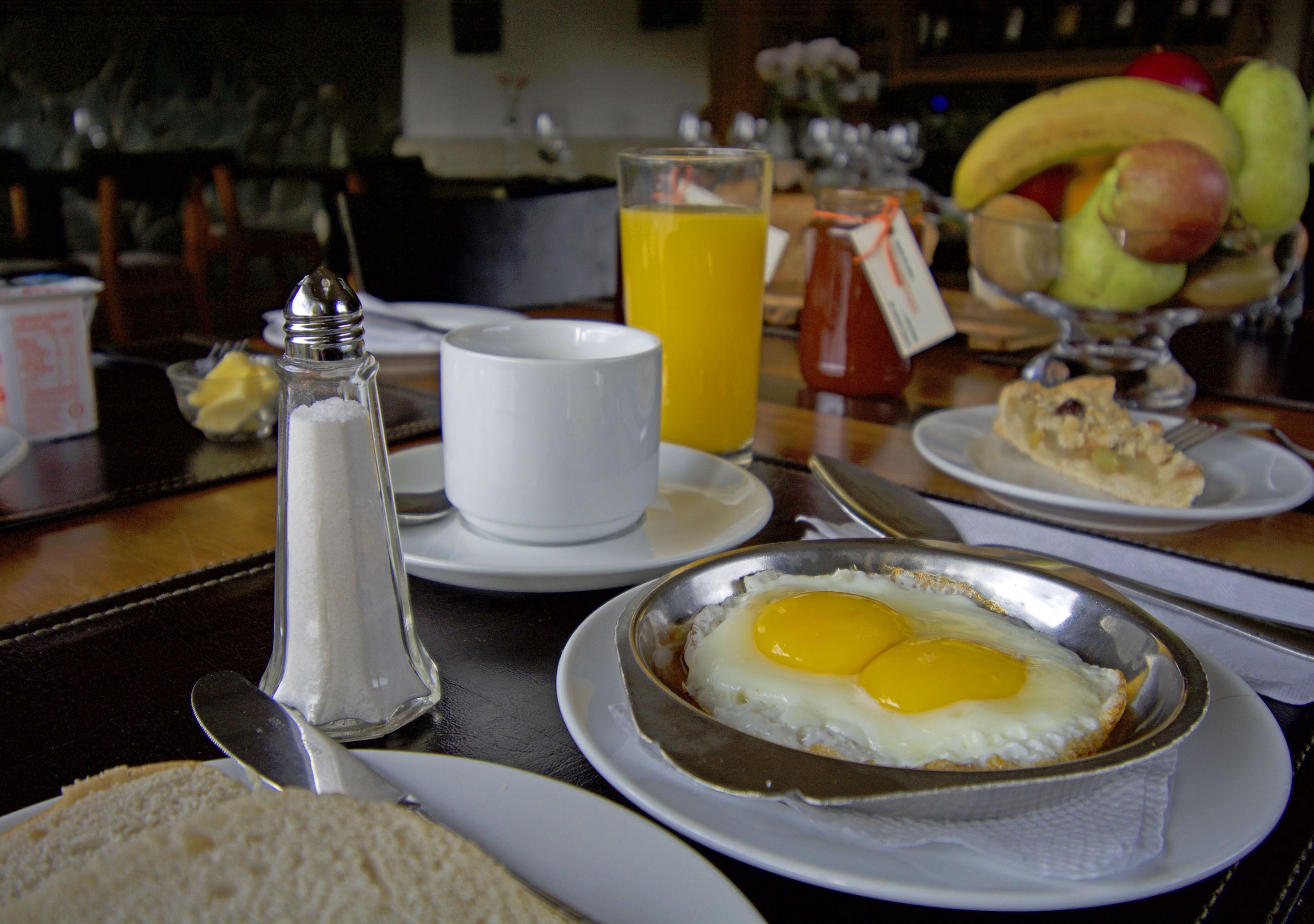 A breakfast setting with eggs, toast, fruit, and juice on a table.