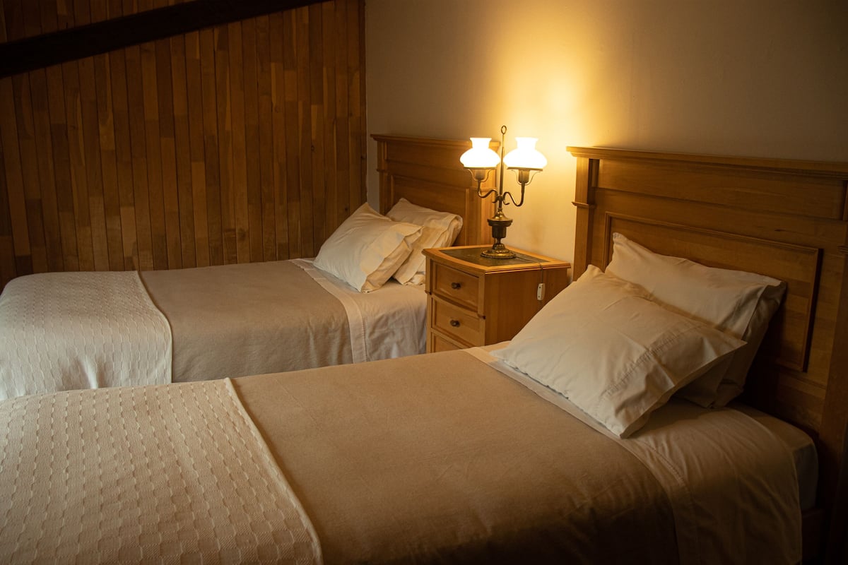 Uma cama de casal com cabeceira de madeira, uma mesa de cabeceira com abajur e um painel de parede em madeira.