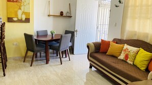 A living room with a brown sofa, a dining table with chairs, a door, and a wall with a painting. - Villa Apartment in North Coast of Dominican Republic (Cabrera)