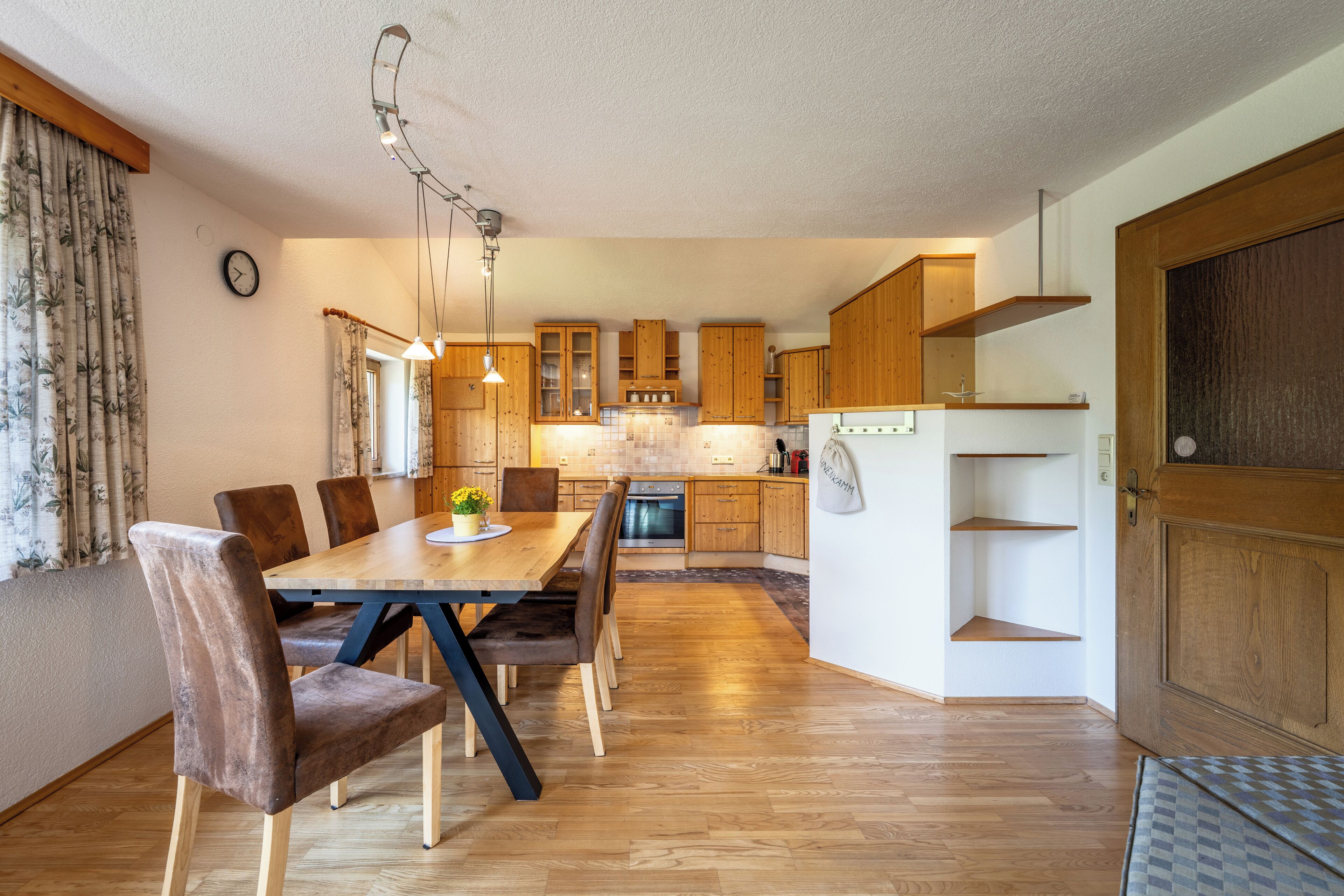 A modern kitchen with wooden cabinets, a dining table with chairs, and a built-in oven.