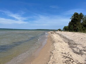 Ein Strand mit klarem Wasser, sandigem Ufer und Bäumen.