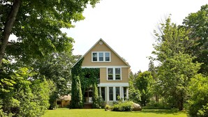 A two-story house with a front porch, surrounded by a well-maintained lawn and trees. - 4+ acres with 100 feet of sugar sand beach on Lake Huron (Cheboygan)