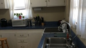 Una cocina compacta con armarios blancos, una encimera azul, un microondas, un lavabo y un taburete pequeño.