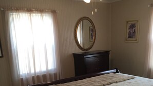 Un dormitorio con cama, cómoda, espejo y ventana con cortinas.