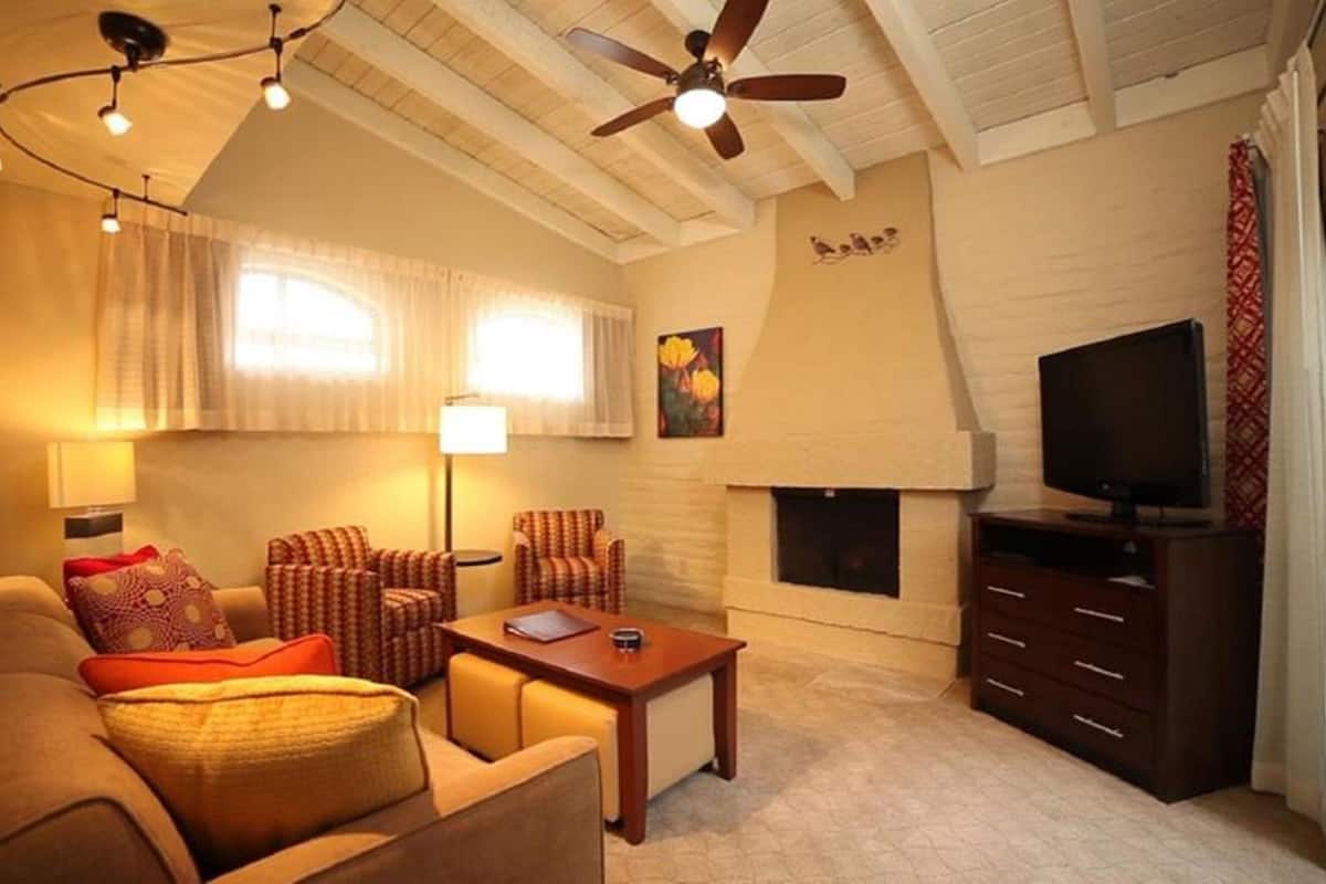 A cozy living room with a sofa, armchairs, a coffee table, a fireplace, a television, and ceiling fans.