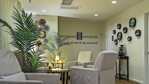 A spa lobby with a large plant, several chairs, a wall with a logo and slogan, and a small table with a lamp.