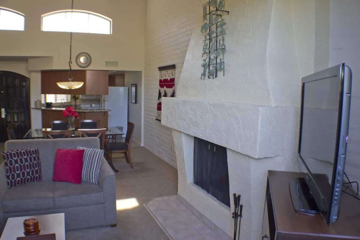 A living room with a fireplace, a sofa, a TV, and a dining area in the background.