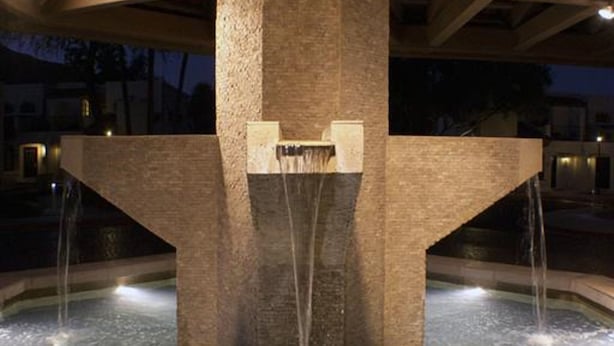 A large stone fountain with water jets under a wooden structure at night.