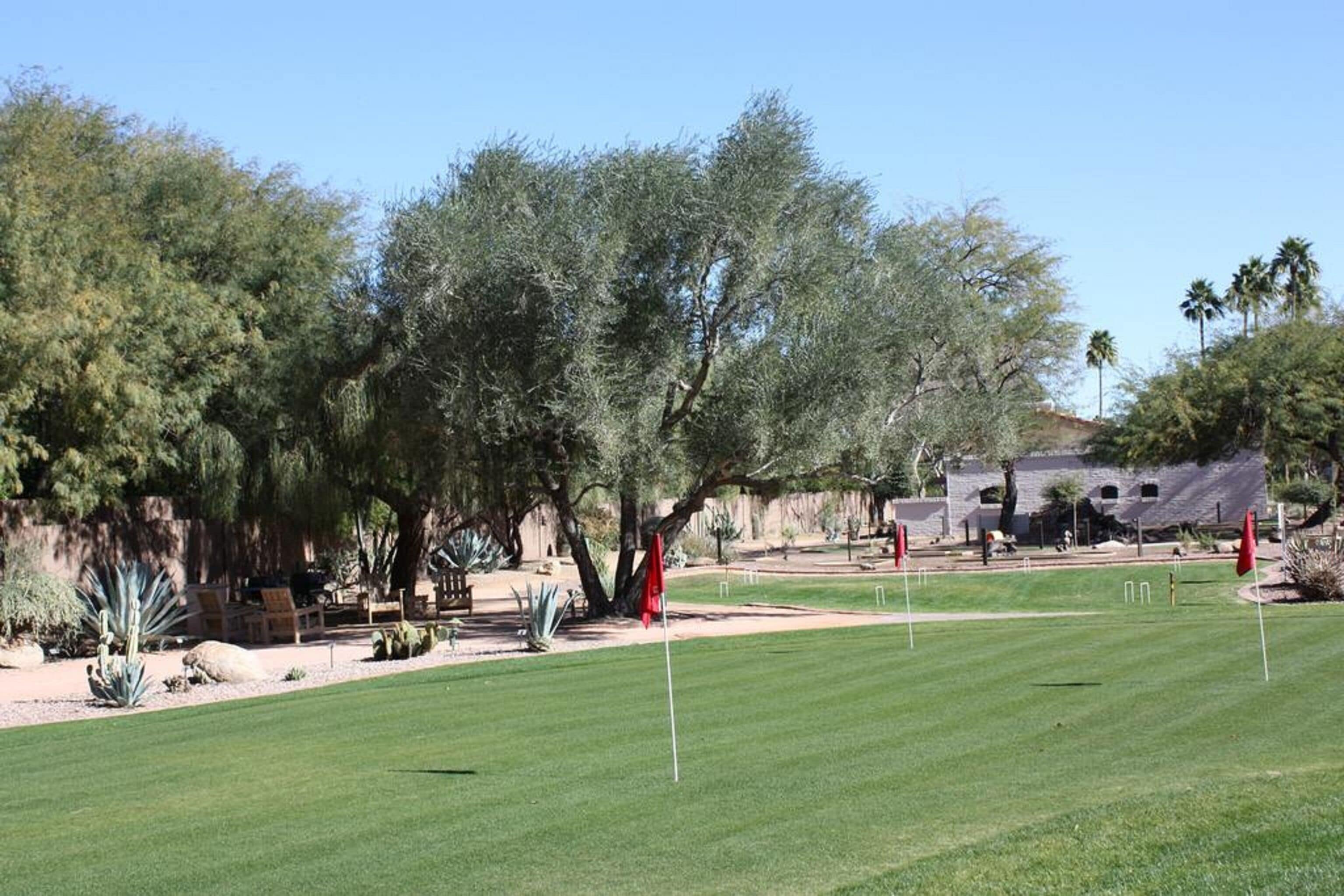 A golf course with a well-maintained lawn, red flags marking the holes, and a variety of trees and shrubs in the background.