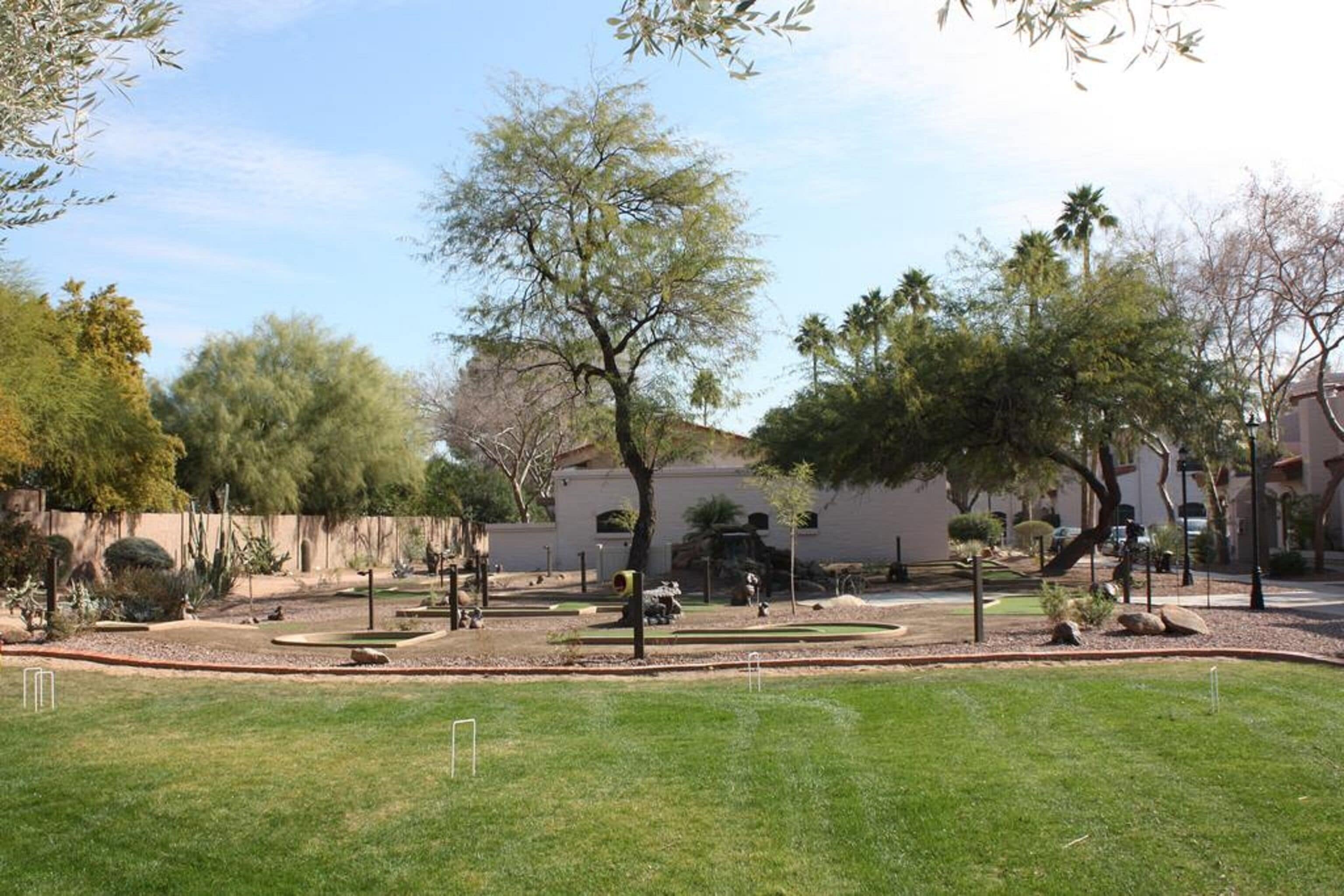 A landscaped garden with a variety of trees and shrubs, a paved area with a fountain, and a building in the background.