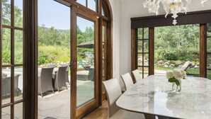 Een eethoek met een marmeren tafel, witte stoelen en een bloemenvaas.