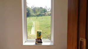 A window with a view of a grassy field and trees. A stack of books is placed on the windowsill. - Delightful Bungalow Near Skibbereen & Baltimore (Skibbereen)