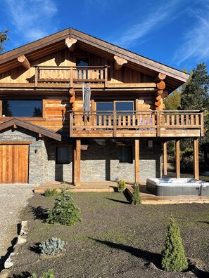 Een houten blokhut met twee verdiepingen, een balkon, stenen fundering en een bubbelbad in de tuin.