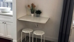 A compact kitchen with a white countertop, a white sink, two white stools, and an air conditioning unit mounted on the wall. - First-Class Crash Pad! studio apartment, close to UCF. (Orlando)