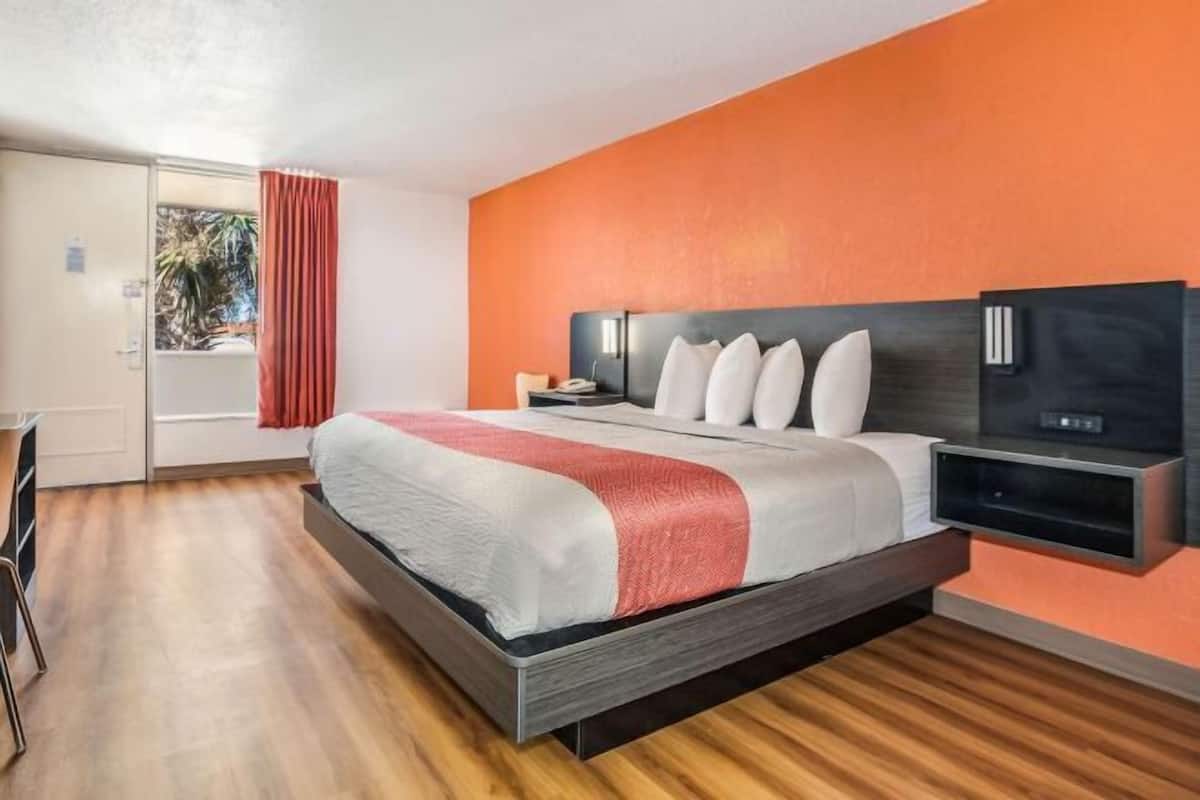 Une chambre d’hôtel moderne équipée d’un lit, d’une table de chevet, d’une télévision et d’une porte coulissante donnant sur un balcon.