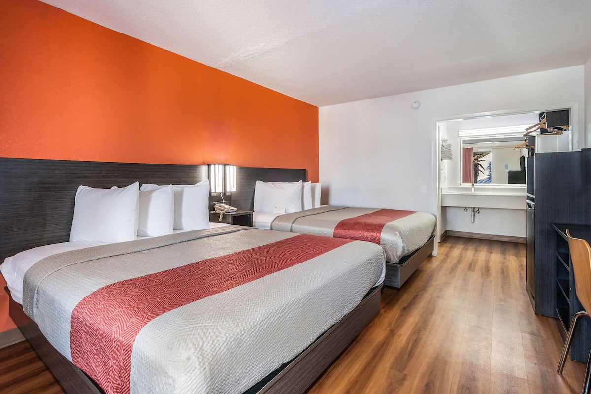 Une chambre d’hôtel avec deux lits, un plancher en bois et un mur d’accent de couleur orange.