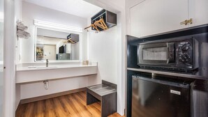 Pieni, käytännöllinen keittiö, jossa on mikroaaltouuni, jääkaappi ja pieni puinen jakkara.