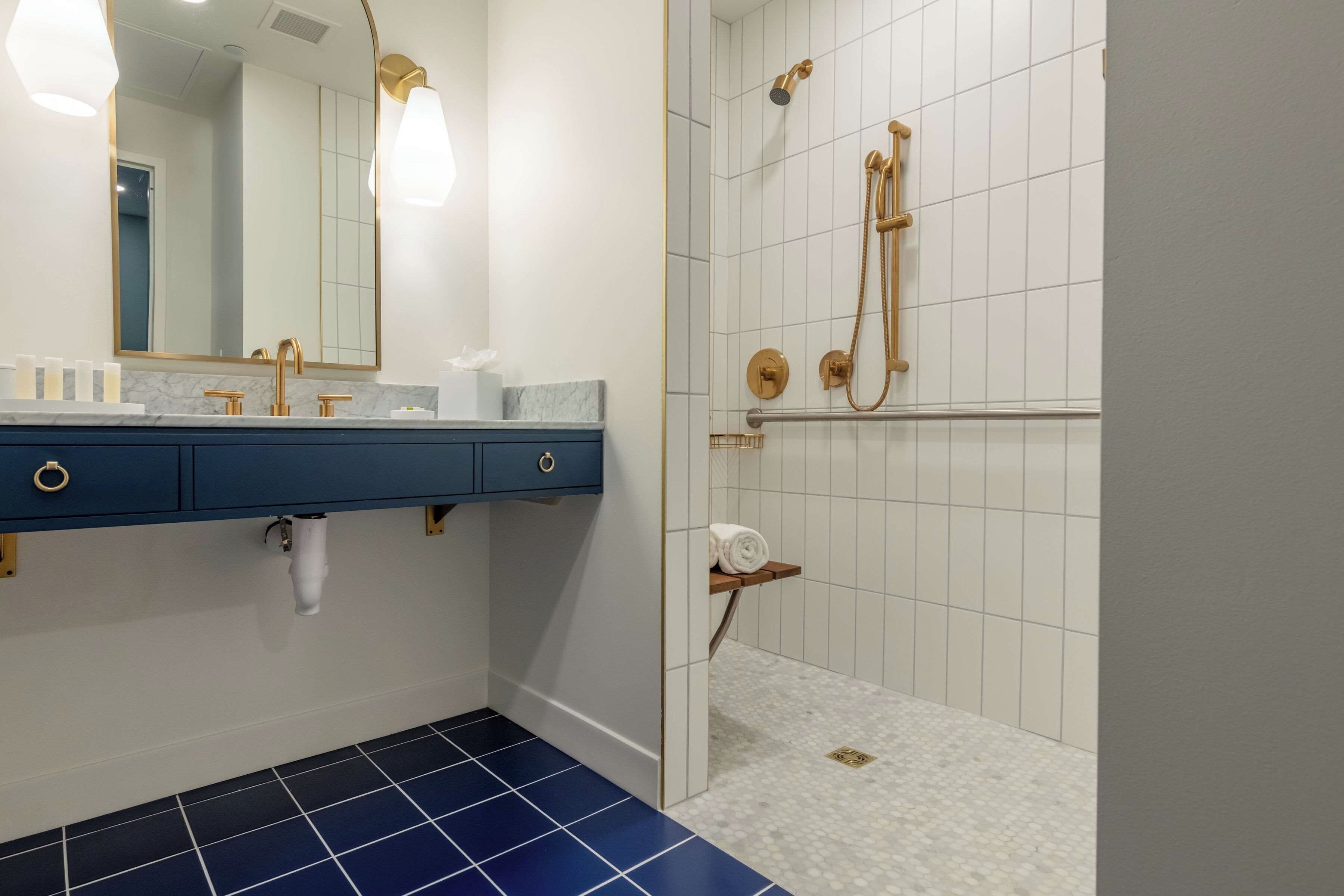 A bathroom with a blue tiled floor, a white sink with gold fixtures, a mirror, and a shower with gold fixtures.