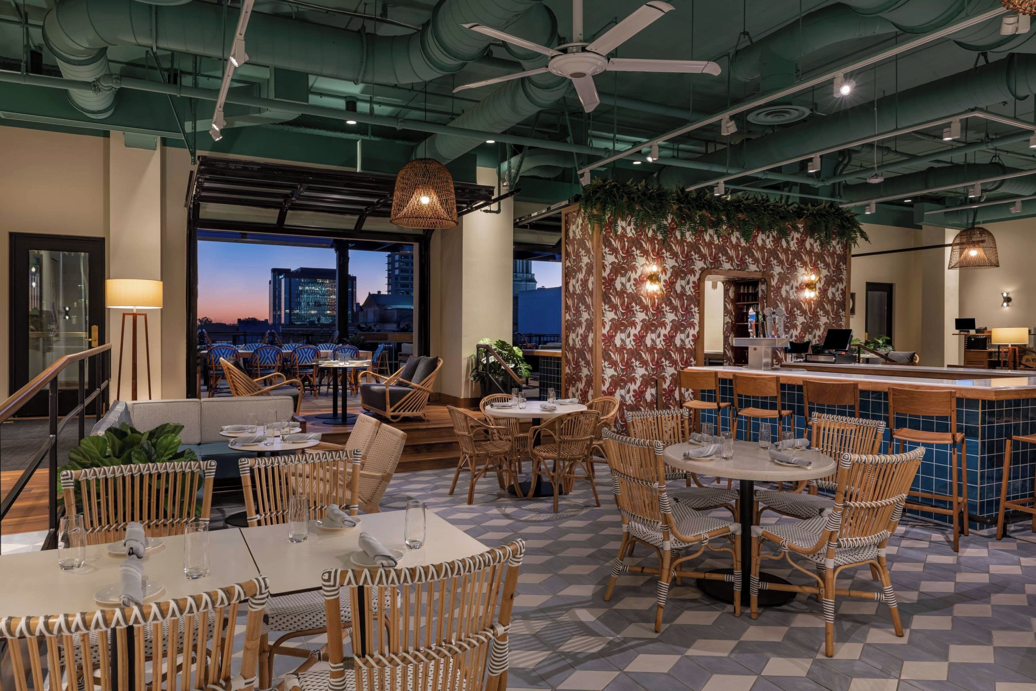 A rooftop restaurant with outdoor seating, city views, and a bar area.