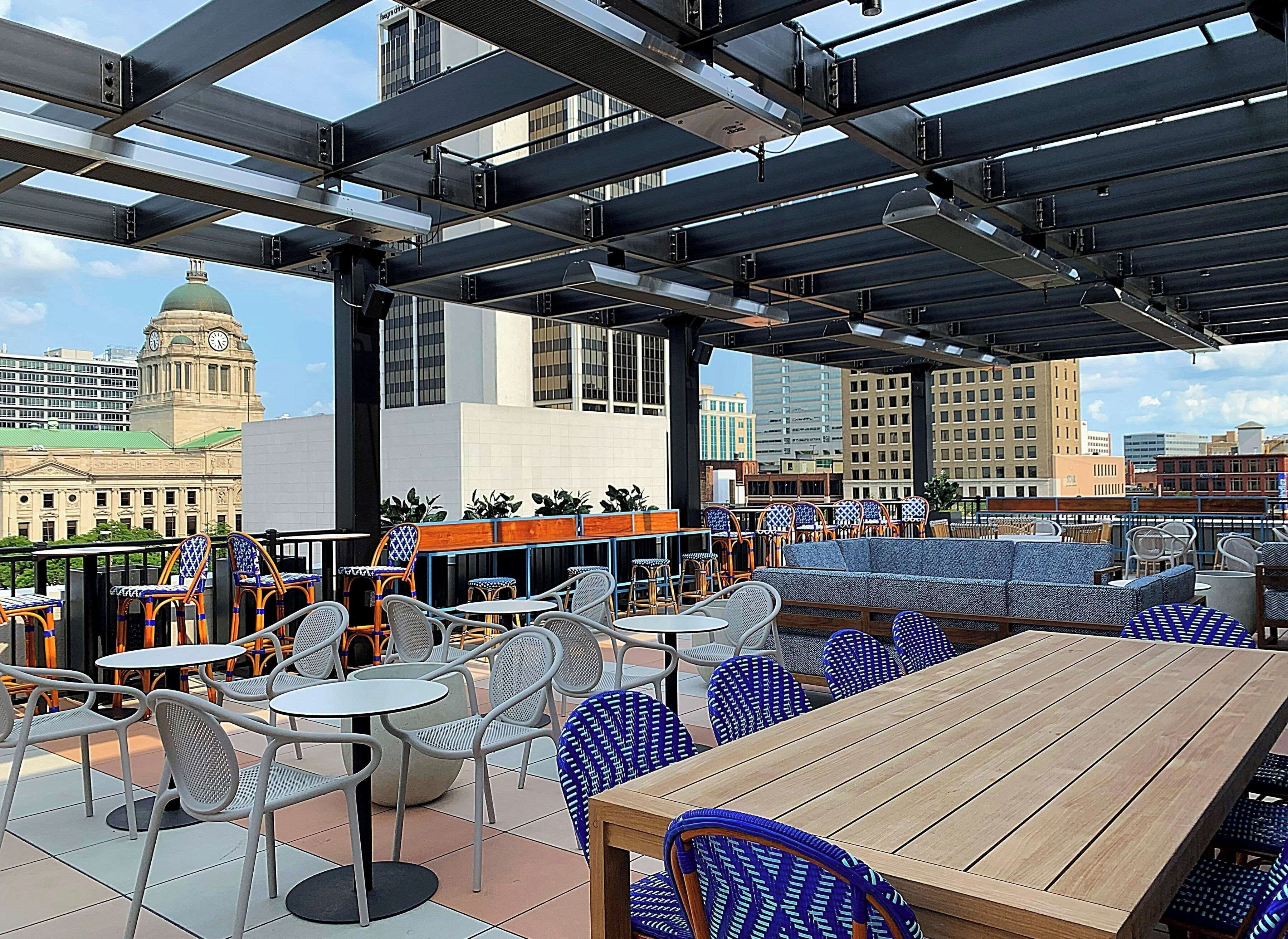 An outdoor seating area with tables and chairs, a wooden table, and a view of a cityscape including a clock tower.