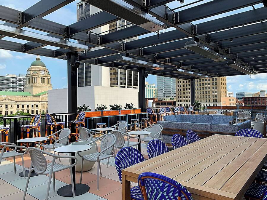 An outdoor seating area with tables and chairs, a wooden table, and a view of a cityscape including a clock tower.