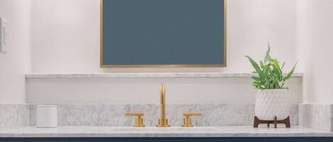A bathroom with a dark blue vanity, a white marble countertop, a gold faucet, and a mirror with a gold frame.