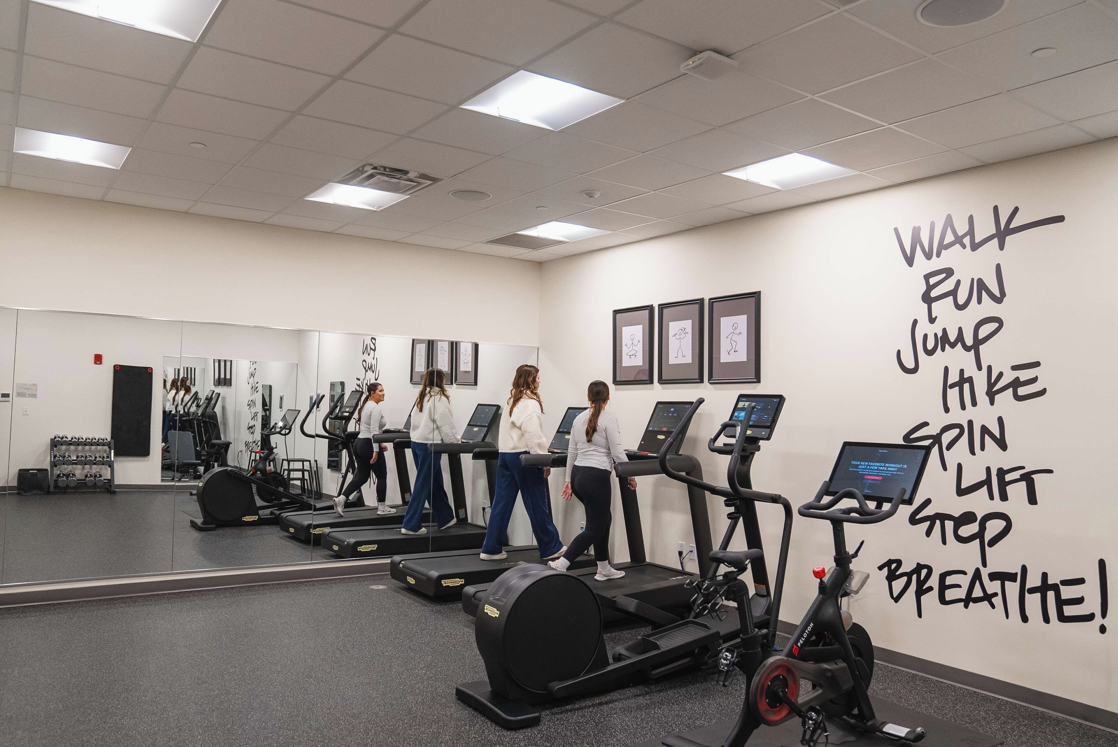 Un gimnasio con cintas de correr, bicicletas estáticas y una pared con frases motivacionales para ejercitarse.