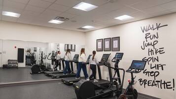 Un gimnasio con cintas de correr, bicicletas estáticas y una pared con frases motivacionales para ejercitarse.