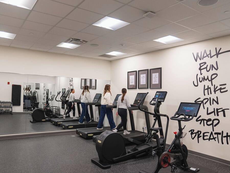 Un gimnasio con cintas de correr, bicicletas estáticas y una pared con frases motivacionales para ejercitarse.